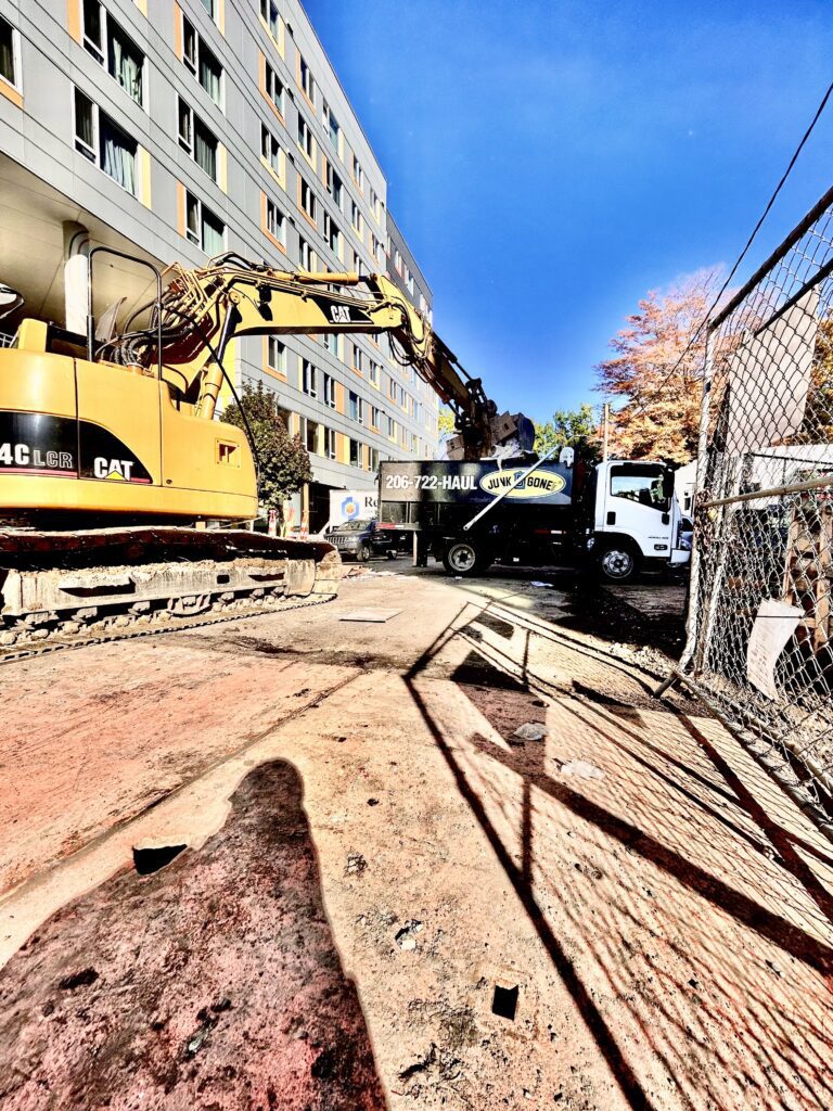 This photo shows an excavator loading construction materials into the bed of a Junk B Gone dump truck