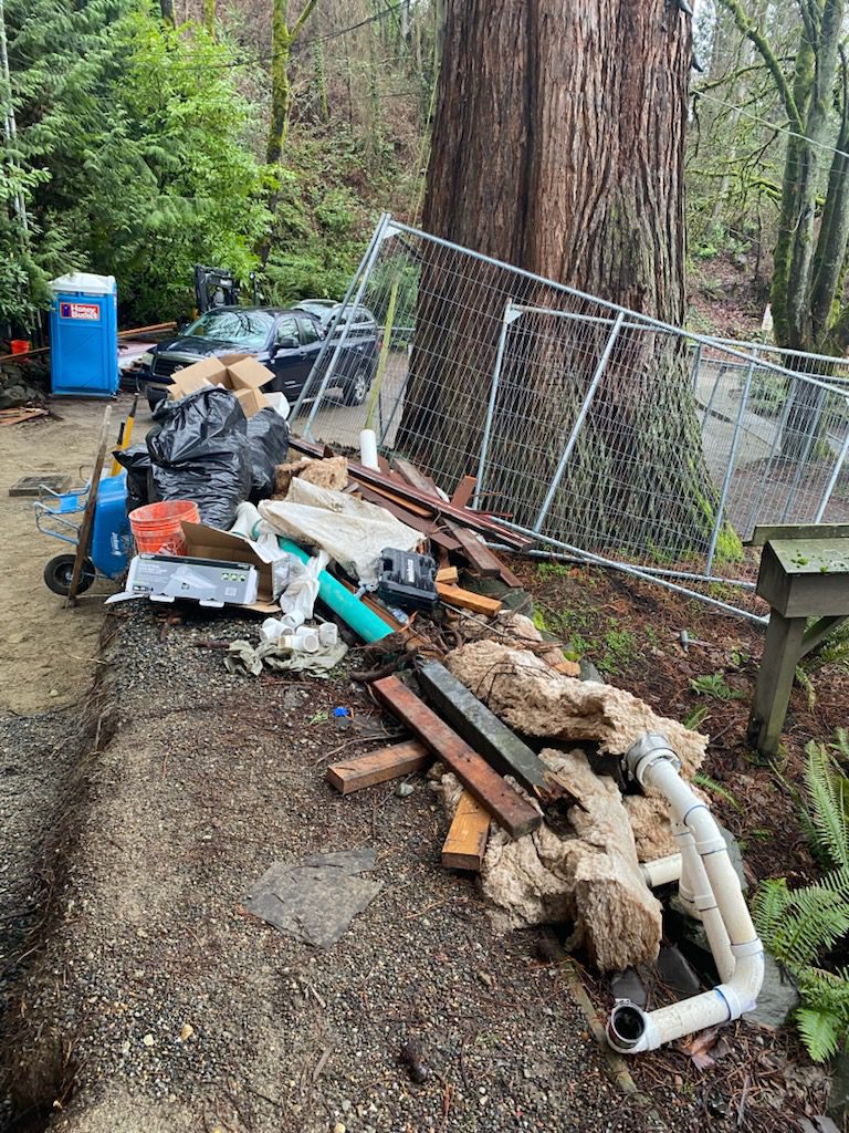 Construction debris including lumber pipes and mixed materials piled in a fenced yard