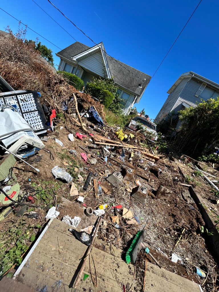 Steep Seattle hillside yard buried end-to-end in scattered junk and debris before Junk B Gone cleared it